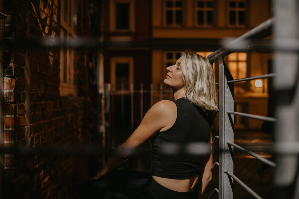 Annika Brönstrup sitzt am Treppengeländer gelehnt auf den Stufen; Gesicht im Profil, Augen geschlossen, gelöst